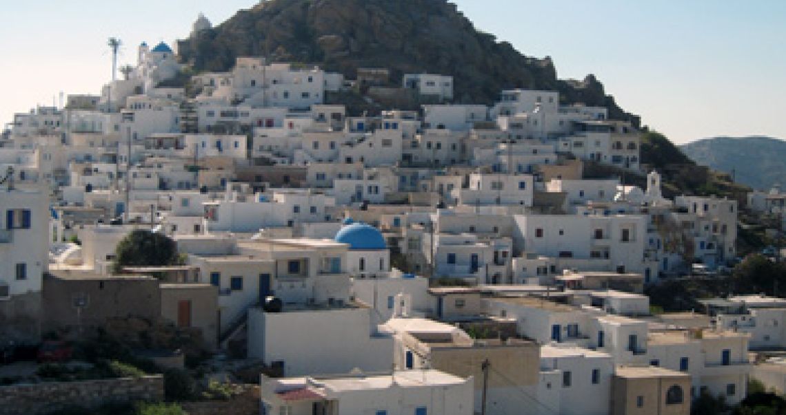 Panoramic view of the traditional white-washed houses and blue-domed churches of Chora, Ios, nestled on the hillside.