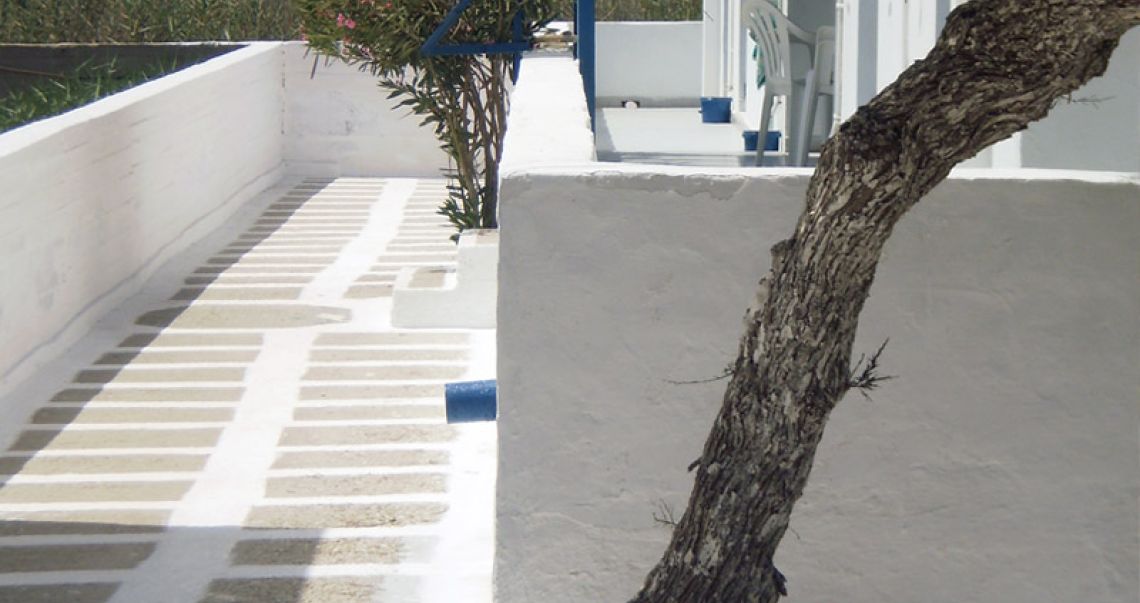 Traditional Cycladic outdoor walkway with white-painted stone paving and a rustic tree trunk detail.