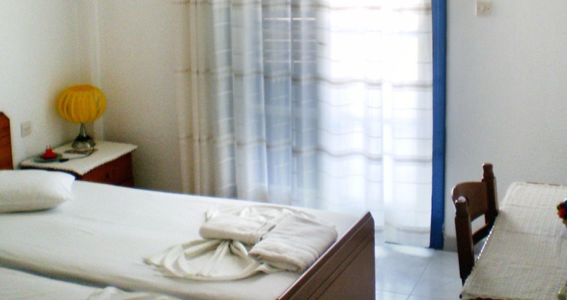 Cozy twin room with a decorative yellow lamp, a wooden workspace, and large glass doors leading to a balcony.
