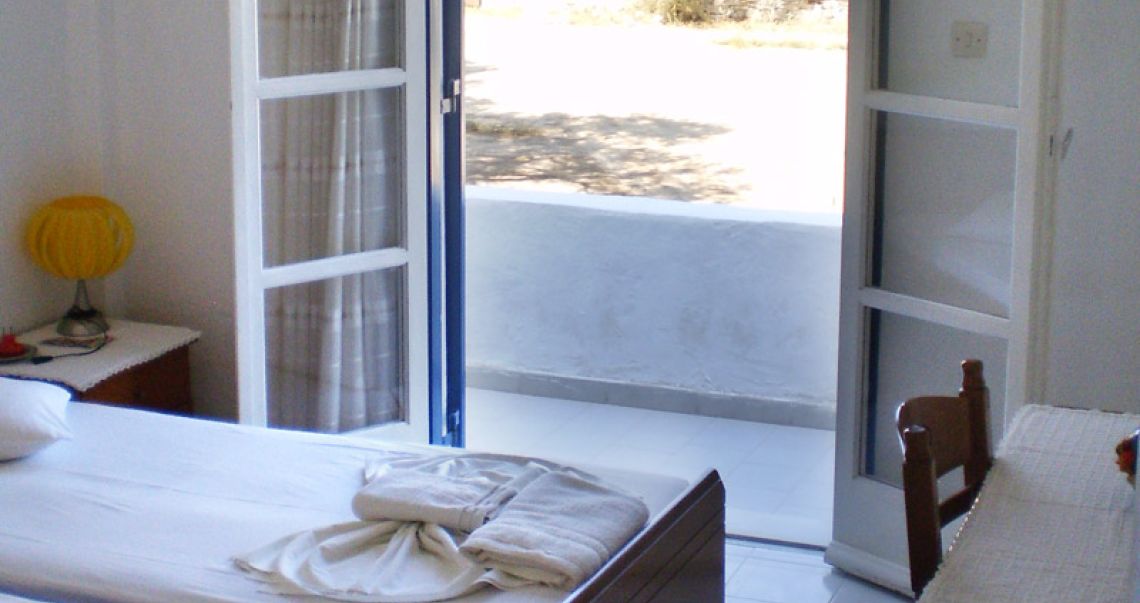 Open balcony doors in a guest room, offering a seamless transition between the cool interior and the sunlit outdoor terrace.