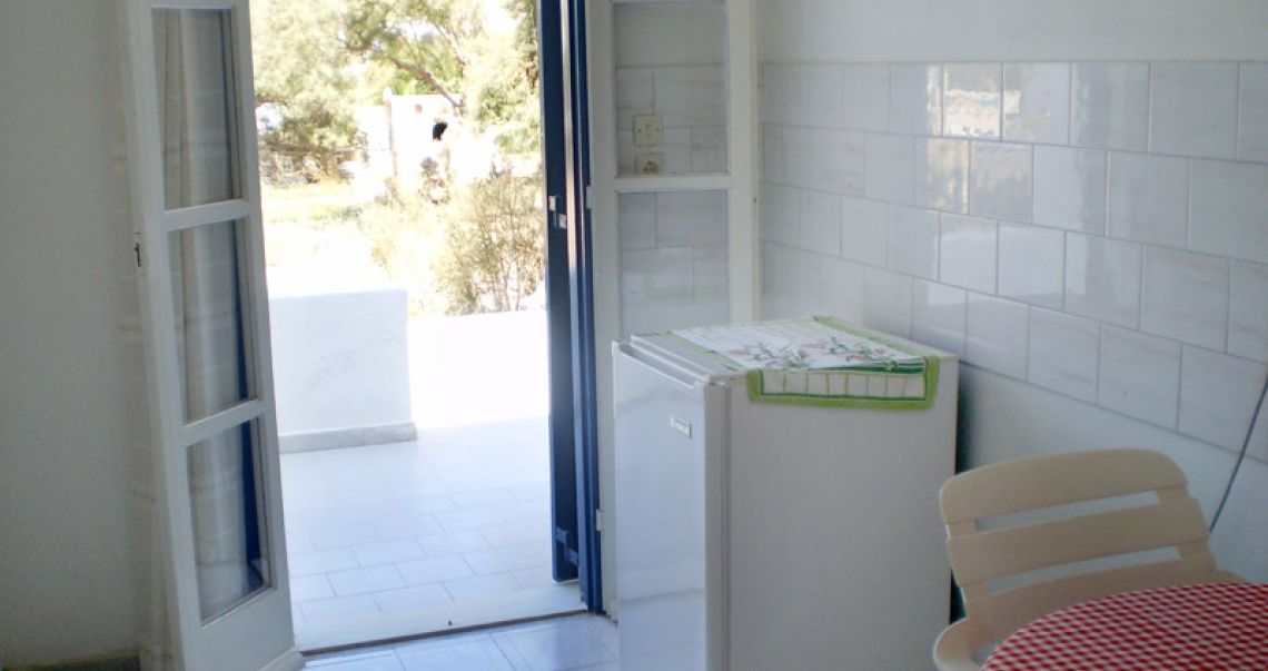 Convenient kitchenette corner with a mini-fridge, a red checkered dining table, and direct access to an outdoor area.