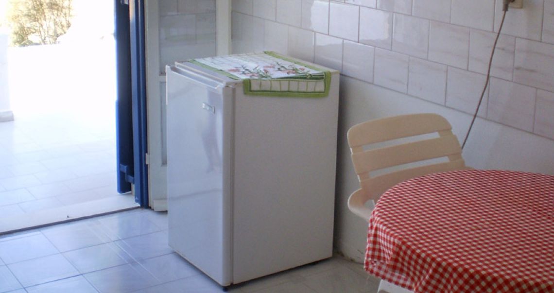 Convenient kitchenette corner with a mini-fridge, a red checkered dining table, and direct access to an outdoor area.