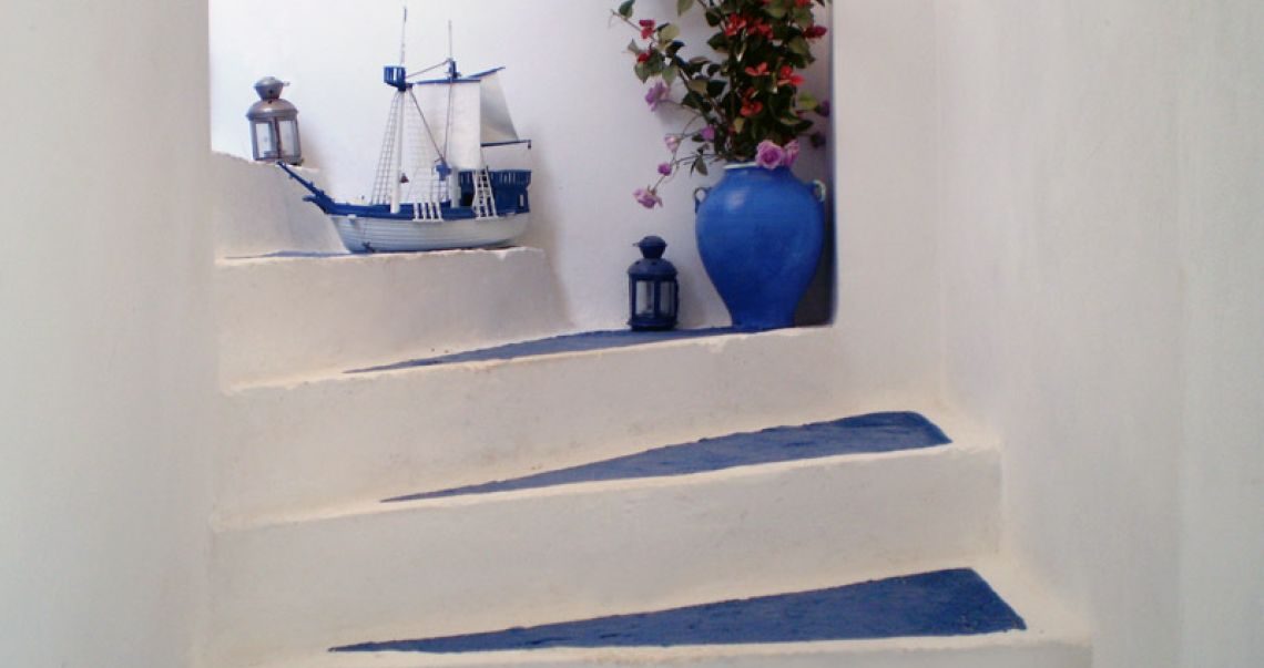 Beautifully decorated white-washed staircase with blue treads, featuring a model ship, a blue vase with flowers, and lanterns.