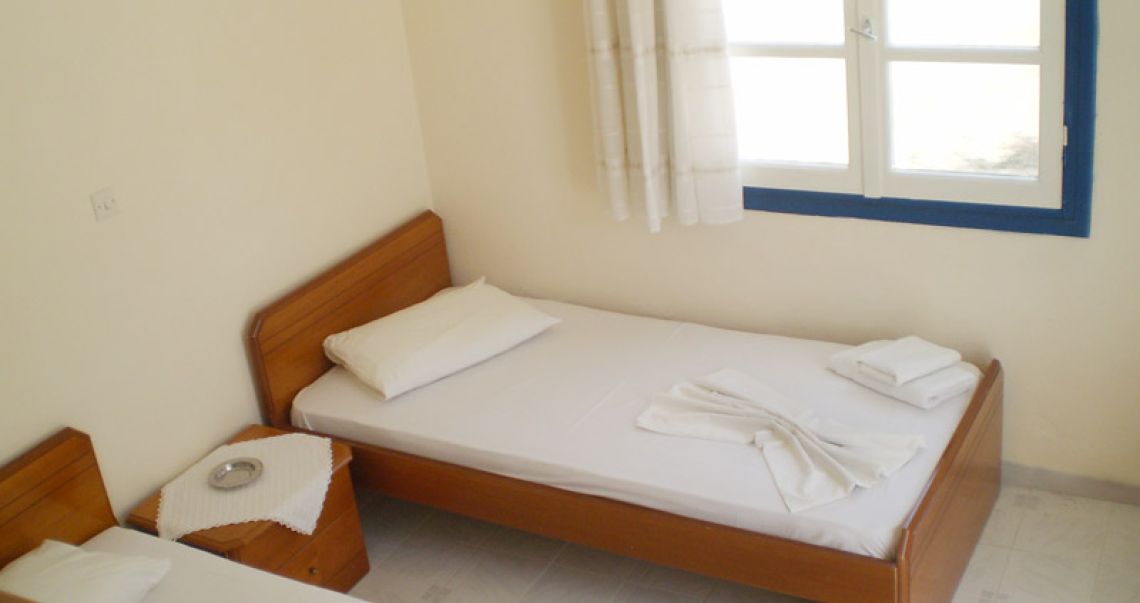 Traditional twin bedroom with wooden bed frames, crisp white linens, and a sunlit window with classic blue shutters.