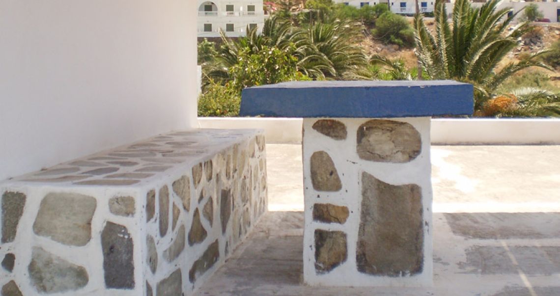 Outdoor seating area featuring a traditional stone-built bench and a blue-topped table with a view of palm trees and hills.