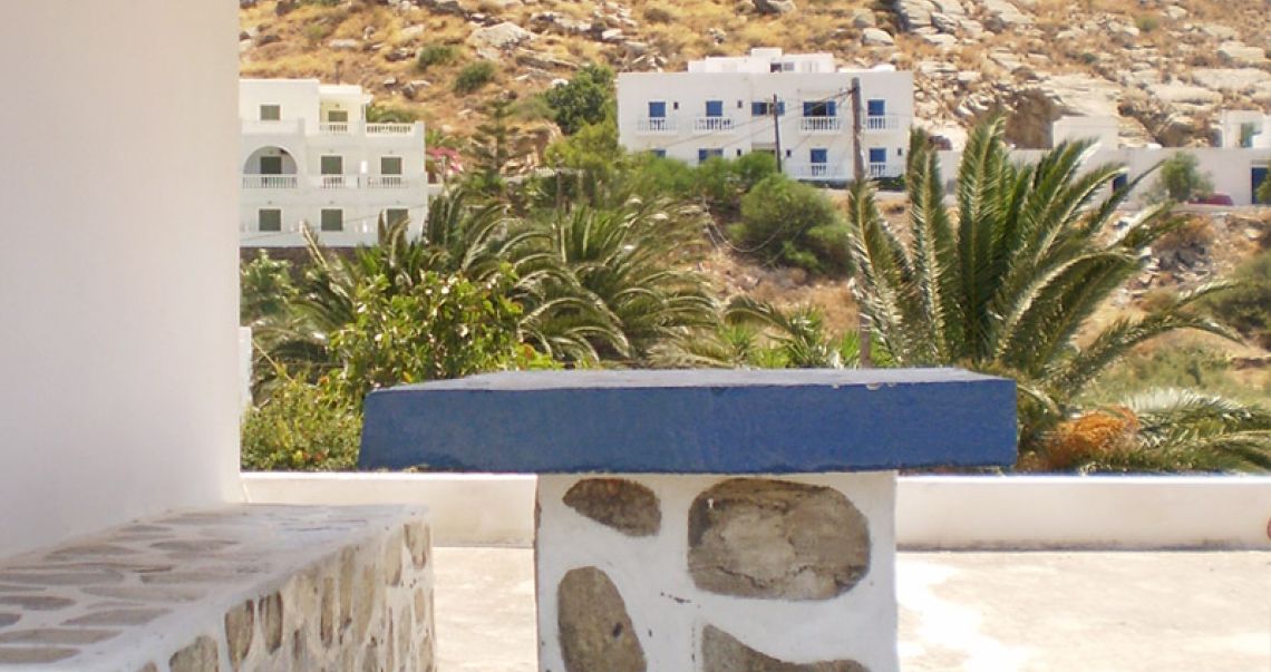 Outdoor seating area featuring a traditional stone-built bench and a blue-topped table with a view of palm trees and hills.