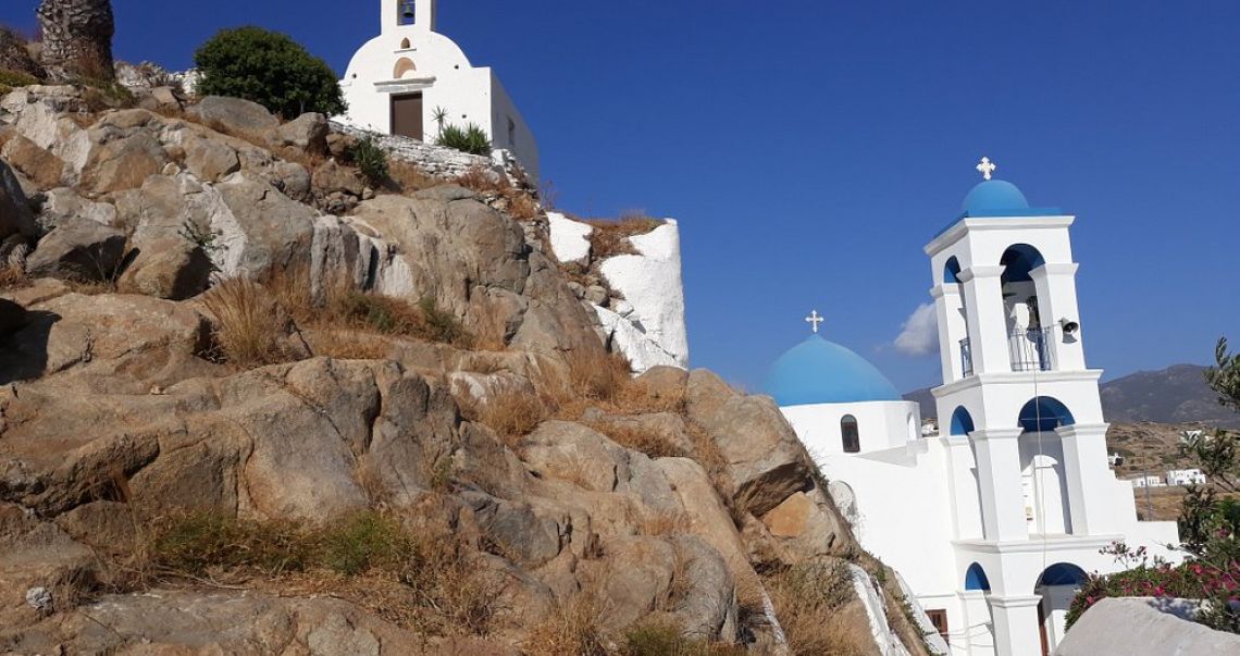 Scenic view of iconic blue-domed churches and white bell towers on a rocky hillside under a clear blue sky in Ios.