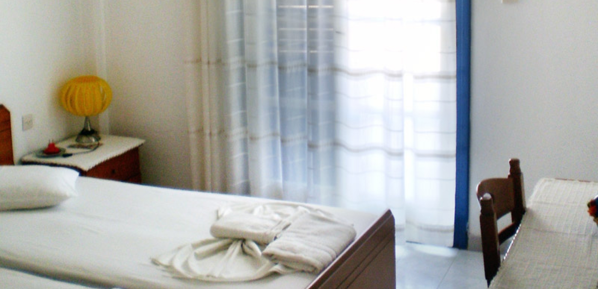 Cozy twin room with a decorative yellow lamp, a wooden workspace, and large glass doors leading to a balcony.