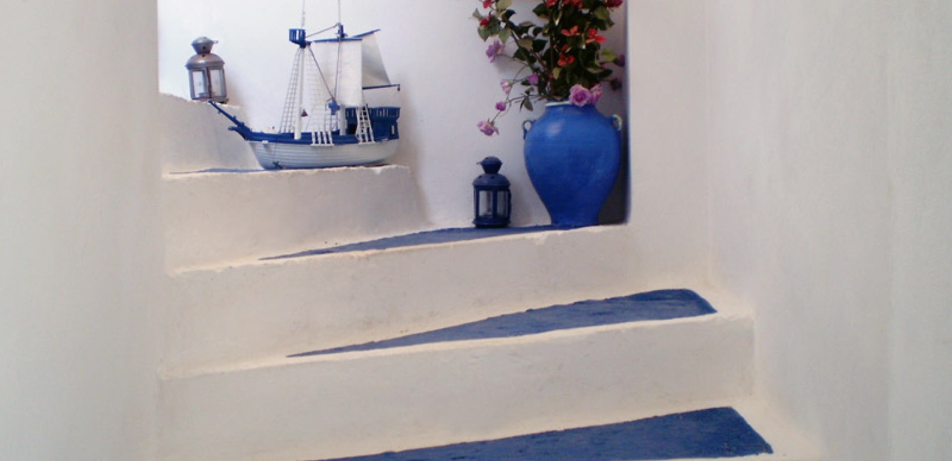 Beautifully decorated white-washed staircase with blue treads, featuring a model ship, a blue vase with flowers, and lanterns.