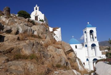 Scenic view of iconic blue-domed churches and white bell towers on a rocky hillside under a clear blue sky in Ios.